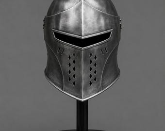 May include: A silver-colored knight's helmet with a visor and diamond-shaped ventilation holes. The helmet is displayed on a black stand against a gray background. The helmet's design is reminiscent of medieval armor.