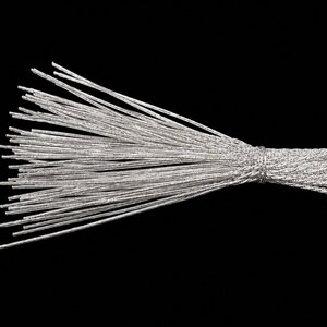 May include: A bundle of thin, silver-colored metallic wires arranged in a fan shape. The wires are gathered and secured at one end with a tightly wrapped silver wire tie, creating a tapered handle effect while the opposite ends remain loose.