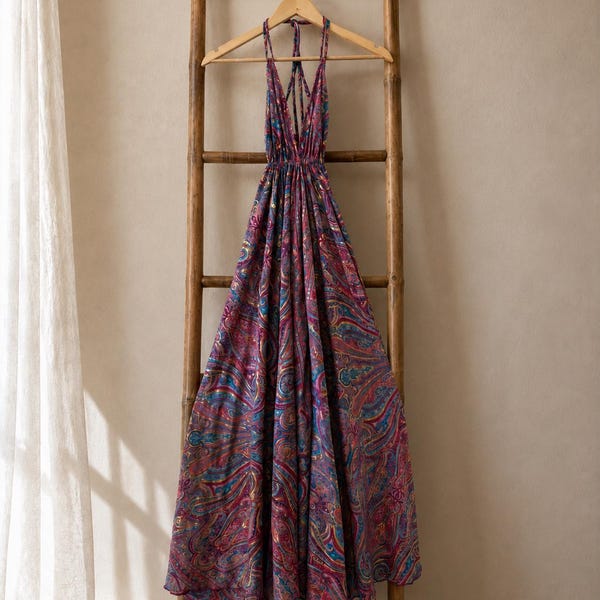 Peut inclure: Une robe longue dos nu avec un motif cachemire vibrant dans des tons magenta, violet, bleu et doré. Le vêtement présente un décolleté en V profond, de fines bretelles croisées dans le dos et une taille froncée avec une jupe ample.