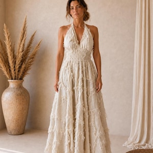 Può includere: Un abito lungo all'americana color beige con profondo scollo a V, vita elasticizzata arricciata e gonna a balze. Il tessuto è decorato con dettagli patchwork a bordi sfrangiati su tutto il corpetto e sulla gonna ampia.