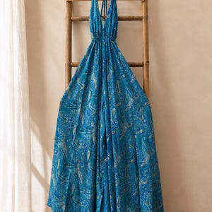Può includere: Una tuta lunga blu caratterizzata da un vivace motivo paisley nei toni del verde acqua e del blu navy con accenti dorati. Il capo presenta un profondo scollo a V, sottili spalline allacciate al collo e una linea a gamba larga.