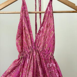 May include: A pink halter top with a deep V-neck and a paisley pattern. The top is hanging on a wooden hanger. The fabric has a flowing, lightweight appearance.