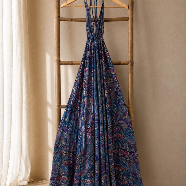 Peut inclure: Une robe longue dos nu avec un motif cachemire aux tons bleu, violet et magenta. Le vêtement présente un décolleté en V profond, de fines bretelles à nouer autour du cou et une jupe longue et fluide tombant depuis la taille cintrée.