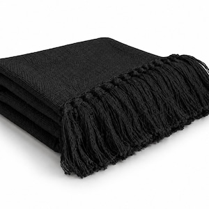 Könnte beinhalten: Eine gefaltete schwarze Wohndecke mit einem strukturierten geometrischen Muster auf der Oberfläche und langen, dekorativen Fransen an der Kante. Der Stoff weist durchgehend eine einheitliche matte schwarze Farbe auf.