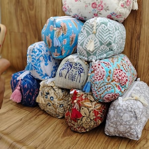 May include: A selection of patterned cosmetic bags in various colours. The bags display floral, leaf, and geometric patterns in shades of blue, red, and white. Each bag has a zip closure and a tassel.