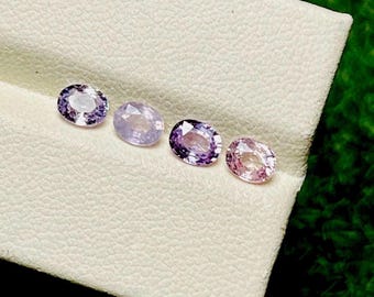 Puede incluir: Cuatro piedras preciosas de corte ovalado en tonos morados y rosas se exhiben sobre una superficie blanca. Las piedras preciosas varían en intensidad de color, desde lavanda pálido hasta violeta intenso. Las gemas están dispuestas en fila.