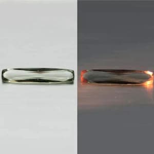 May include: A clear, rectangular glass object with rounded edges. The object is shown in two different lighting conditions, with a bright white background on the left and a dark gray background with an orange glow on the right.