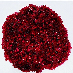 Puede incluir: Un montón de pequeñas gemas facetadas de color rojo intenso. Las gemas están densamente empaquetadas, creando una superficie texturizada y brillante. La forma general es aproximadamente circular sobre un fondo blanco.