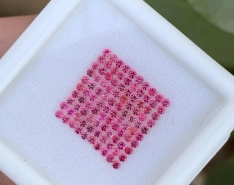 Puede incluir: Una colección de pequeñas gemas rosas redondas dispuestas en forma de diamante dentro de un recipiente cuadrado blanco. Las gemas varían en tonalidad de rosa claro a oscuro.