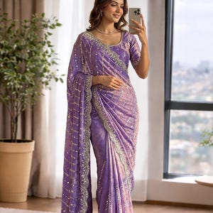 Peut inclure: Un sari lavande avec des détails de sequins complexes et un chemisier assorti. Le sari présente une bordure décorative et est drapé avec élégance. L'image montre une femme portant le sari, mettant en valeur le design et la coupe.