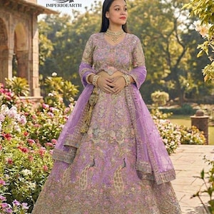 May include: A lavender-colored, embroidered formal gown with a matching sheer scarf. The gown features intricate gold detailing and peacock motifs. The model is wearing gold jewelry, including a necklace and bracelets. The logo "IMPERIOEARTH" is visible in the upper left corner.