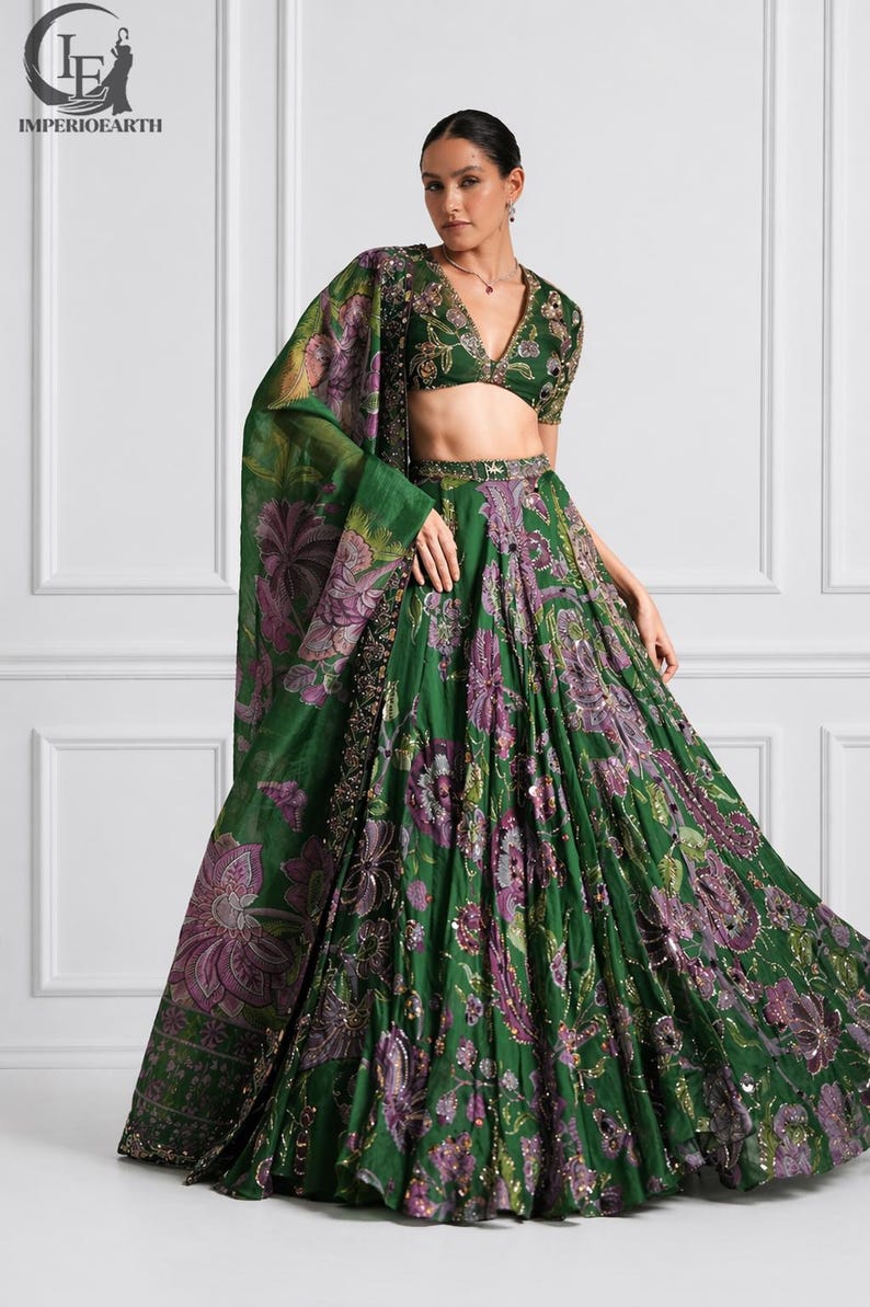 May include: A green floral print lehenga set with a matching dupatta. The set features a V-neck blouse with intricate embroidery and a full, flowing skirt. The floral pattern includes purple and gold accents.