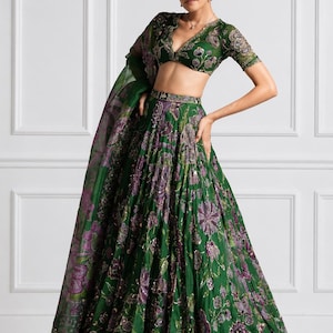 May include: A green and purple floral embroidered lehenga choli set. The set includes a short-sleeved top with a plunging neckline, a long skirt, and a matching dupatta. The outfit is embellished with sequins and intricate embroidery.