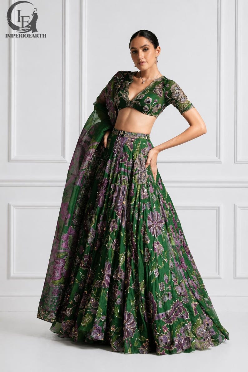 May include: A green and purple floral embroidered lehenga choli set. The set includes a short-sleeved top with a plunging neckline, a long skirt, and a matching dupatta. The outfit is embellished with sequins and intricate embroidery.