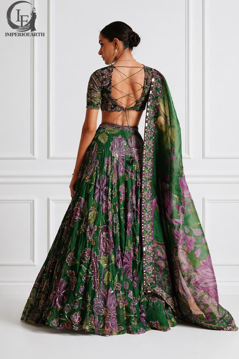 May include: A green floral print lehenga with a matching blouse and dupatta. The lehenga features a full skirt with purple and gold accents. The blouse has a lace-up back. The dupatta has a floral pattern and a beaded border.