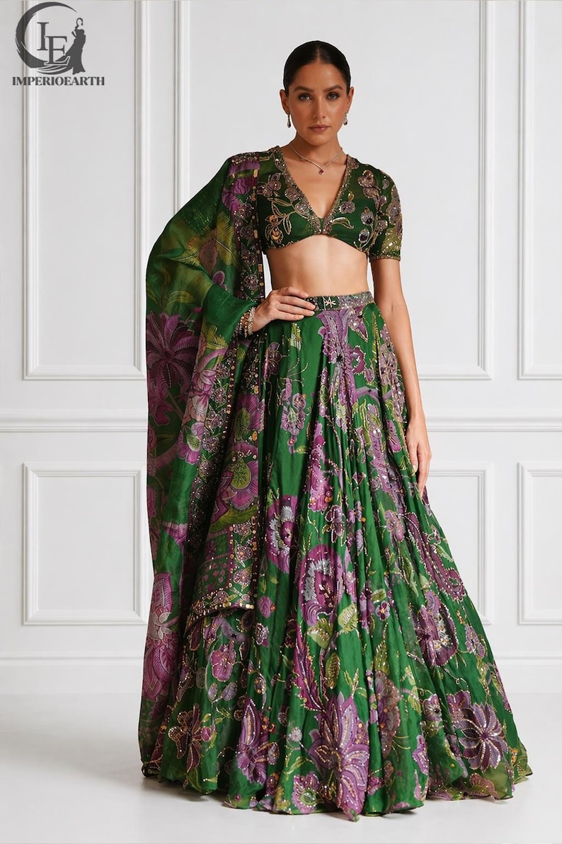 May include: A green and purple floral print lehenga set. The set includes a short-sleeved top, a long skirt, and a matching shawl. The outfit is embellished with gold sequins. The logo "IMPERIOEARTH" is in the top left corner.