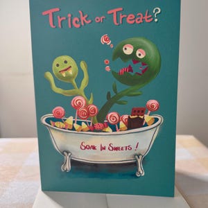 May include: A teal greeting card featuring two green monsters in a white claw-foot bathtub filled with various candies. The text at the top reads Trick or Treat? and the text on the side of the bathtub reads Soak In Sweets! The illustration includes lollipops, candy corn, and chocolate bars.