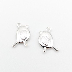 May include: Two silver-toned metal bird charms, each featuring a smooth body, a textured wing detail, and a small circular loop at the top for attachment. The charms are shaped like small, rounded birds with a pointed beak and a tail.