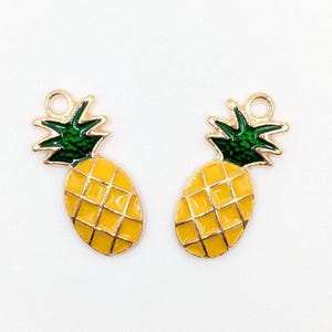 May include: Two gold-coloured pineapple charms with yellow enamel bodies and green enamel tops. The charms have a small loop at the top for attaching to jewellery or other crafts. The pineapple design is a popular tropical motif.
