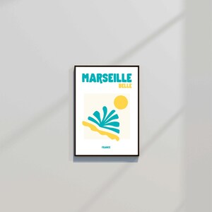 May include: A framed art print featuring the words "MARSEILLE BELLE" in turquoise above a yellow sun and abstract turquoise and yellow shapes. The word "FRANCE" is printed below the image.