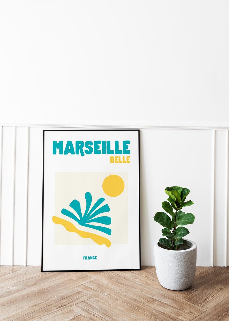 May include: A framed art print with the words "MARSEILLE BELLE" in teal and yellow. The print features a yellow sun, teal and yellow abstract shapes, and the word "FRANCE". A potted plant sits to the right.