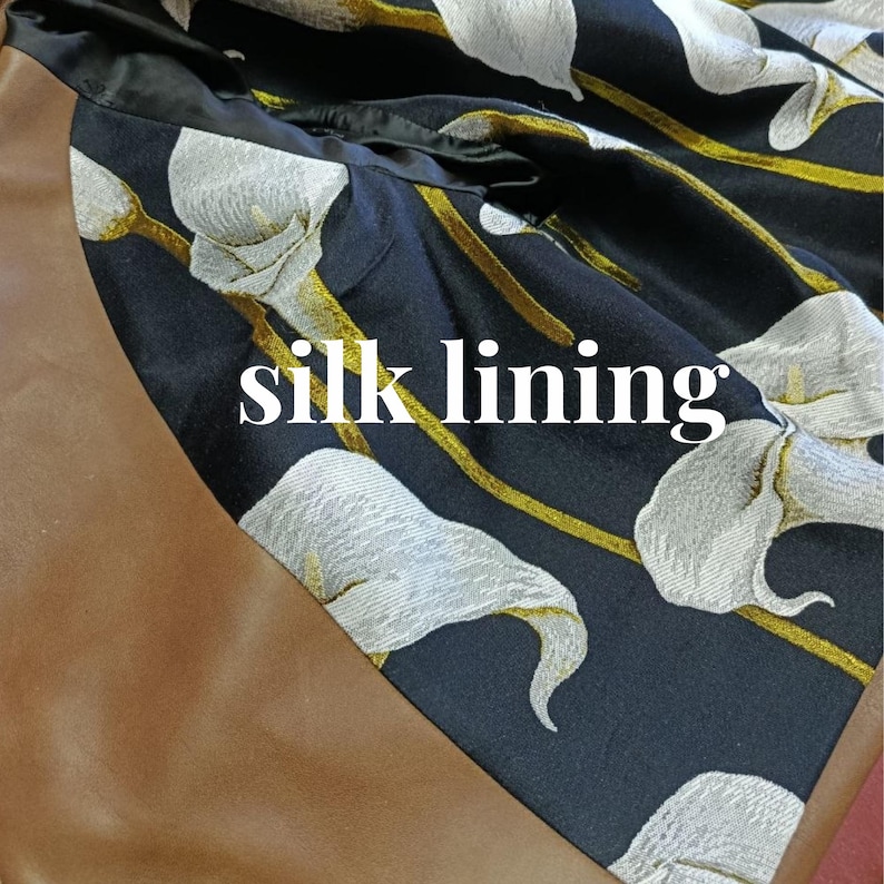 May include: Close-up of a black silk lining with a white floral pattern and gold accents. The text "silk lining" is visible in white. The lining is set against a brown background.