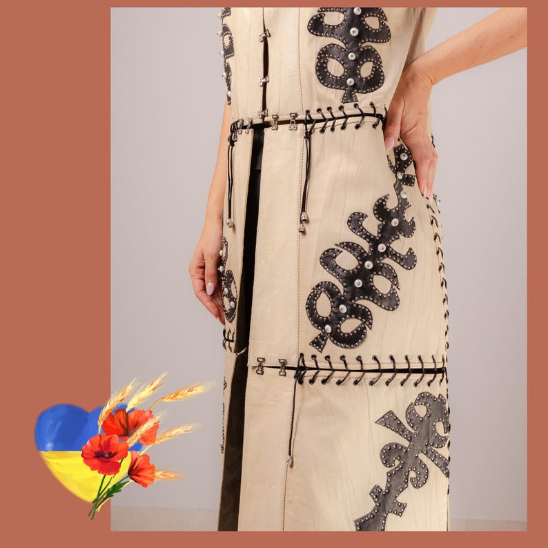 May include: Cream leather vest with black decorative elements and silver studs. The vest has detailed black leather cutouts and small silver embellishments. The design includes a black belt and black trim along the edges.
