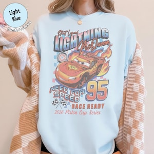 May include: Light blue sweatshirt featuring a graphic of Lightning McQueen from the movie Cars. The design includes the text "Street Legend Lightning McQueen", "Need for Speed", and the number "95". The sweatshirt is labeled "Race Ready" and "2026 Piston Cup Series".