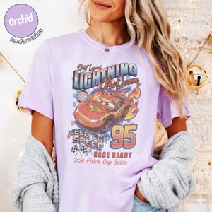 May include: Orchid Comfort Colors t-shirt featuring a graphic of Lightning McQueen from the Cars movie. The design includes the text "Street Legend Lightning McQueen", "Need for Speed", and "95". The shirt is race ready for the 2026 Piston Cup Series.