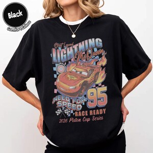 May include: Black t-shirt featuring a graphic of Lightning McQueen from the movie Cars. The design includes the text "Street Legend Lightning McQueen 95 Need for Speed Race Ready 2026 Piston Cup Series". The shirt is labeled "Comfort Colors".