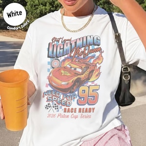 May include: White t-shirt featuring a graphic of Lightning McQueen from the movie Cars. The design includes the text "Street Legend Lightning McQueen", "Need for Speed", and "95". The shirt is labeled "Race Ready" and "2026 Piston Cup Series".