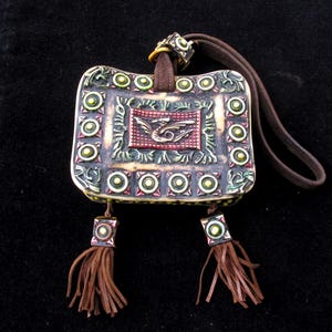 May include: A small, rectangular, decorative pouch with a brown leather strap. The pouch is decorated with green, red, and gold accents and a dragon design. The pouch has two brown tassels.