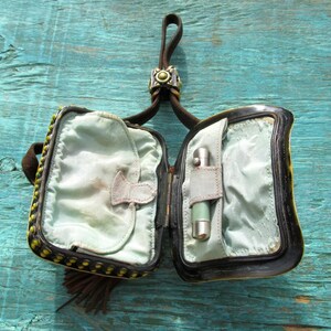 May include: A small black and yellow beaded purse with a brown leather strap and a metal clasp. The purse is open and the inside is lined with a light blue fabric. A small silver lighter is in one of the compartments.