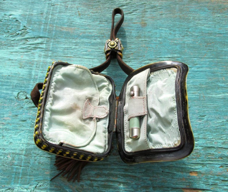 May include: A small black and yellow beaded purse with a brown leather strap and a metal clasp. The purse is open and the inside is lined with a light blue fabric. A small silver lighter is in one of the compartments.