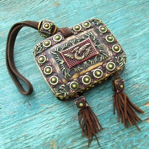 May include: A small, ornate, brown leather pouch with a decorative metal clasp and tassels. The pouch is decorated with gold and green accents and a raised, colorful dragon design.