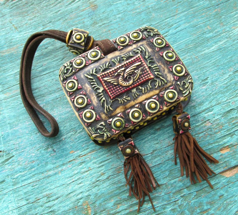 May include: A small, ornate, brown leather pouch with a decorative metal clasp and tassels. The pouch is decorated with gold and green accents and a raised, colorful dragon design.