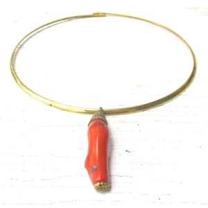 May include: A gold-toned metal collar necklace featuring a single, elongated, smooth, bright orange coral-like pendant. The pendant is capped with a textured, dark metal top and a small, circular, gold-toned metal base at the bottom end.