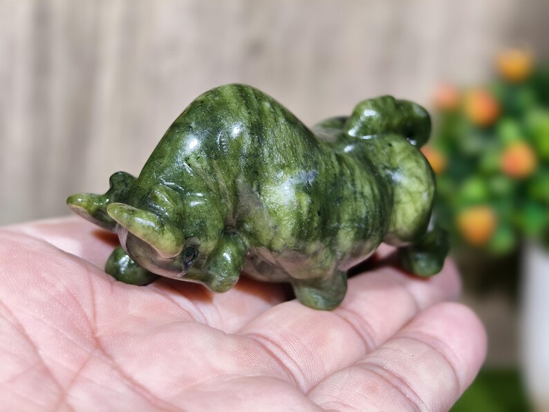 May include: A small, green stone sculpture of a bull. The bull is carved with detailed features, including horns and muscular body. The stone has a marbled appearance with varying shades of green.
