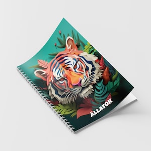 Puede incluir: Un cuaderno de espiral con una ilustración de un tigre multicolor rodeado de follaje tropical estilizado sobre un fondo verde azulado. La palabra ALLATOK está impresa en letras mayúsculas blancas en la esquina inferior derecha de la portada.