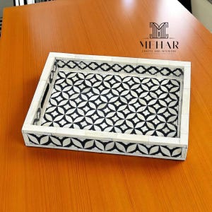 May include: Rectangular decorative tray with a geometric black and white pattern. The tray has a white border with black accents and integrated handles. The tray is made by Mehar Crafts and Interiors.