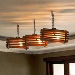 May include: Three wooden pendant lights suspended from the ceiling. Each light fitting is a horizontal cylinder made of wooden slats and bands, with a warm glow from within. The lights are hung by metal chains.