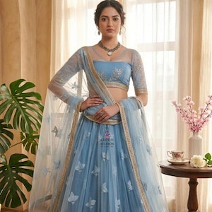 May include: A light blue formal gown with floral embroidery and a sheer overlay. The gown features a matching sheer shawl and gold trim. The top has a sheer neckline and short sleeves. The image includes the text "cloths studios".