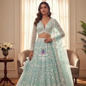 May include: A light turquoise lehenga with detailed white floral embroidery. The outfit includes a long-sleeved, V-neck crop top and a matching dupatta. The skirt has detailed patterns along the hemline. The text "GROTHS STUDIOS" is visible.