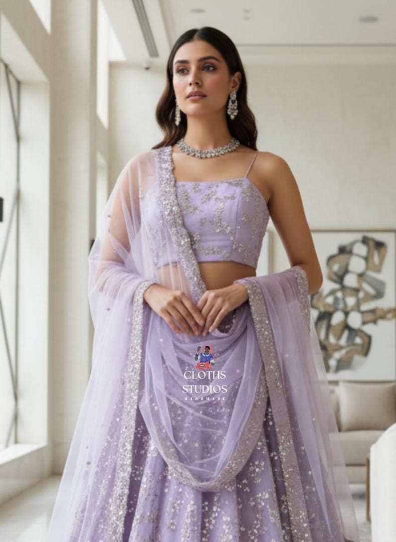 K&ouml;nnte beinhalten: Ein lavendelfarbenes formelles Kleid mit passendem transparentem Schal. Das Kleid hat aufwendige silberne Verzierungen und einen quadratischen Ausschnitt. Das Outfit wird mit einer silbernen Halskette und Ohrringen erg&auml;nzt. Der Text "CLOTHS STUDIOS HANDMADE" ist enthalten.