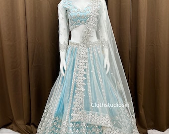 Puede incluir: Un vestido formal azul claro con intrincados bordados y adornos plateados. El vestido presenta un top con cuello en V, mangas largas y una falda fluida. Un chal transparente a juego cae sobre los hombros. El texto "clothstudiosin" es visible.