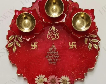 May include: A red decorative plate with three brass bowls, floral accents, and gold script. The plate features a floral design with gold leaf accents and three small brass bowls. The plate has text and symbols in gold.