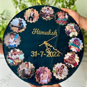 Puede incluir: Un reloj de pared redondo y personalizado con un fondo verde azulado oscuro. El reloj presenta un nombre y una fecha dorados, rodeados de doce pequeños marcos de fotos. Las manecillas del reloj también son doradas.