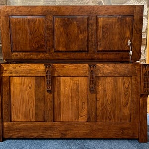 May include: A large wooden chest with a hinged lid, made from dark-stained wood. The chest has decorative carvings on the front and sides, and a metal latch. The lid is partially open, revealing the interior. This antique-style chest is a storage solution.