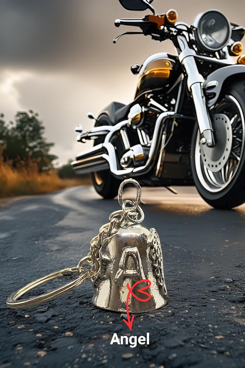 May include: A silver motorcycle bell with the word "Angel" and the letter "A" on the side. The bell is attached to a chain and a ring. A black and gold motorcycle is in the background.