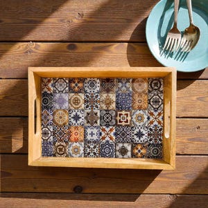 May include: A rectangular wooden serving tray with a mosaic tile design. The tray features a light brown wooden frame and handles. The tile design is composed of various square tiles with intricate patterns in shades of blue, brown, orange, and white.